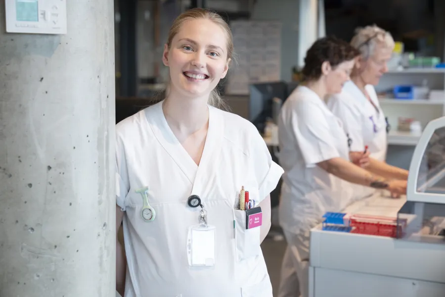 Dame som står i hvite sykehusklær og smiler
