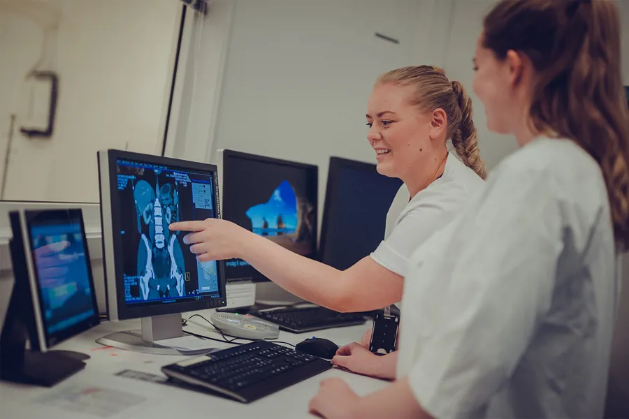 To radiologer smiler og peker på skjerm