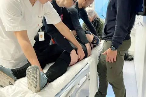 Fem personer som hjelper pasient i seng