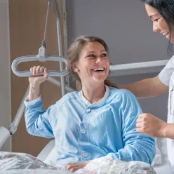 Pasient som ligger i seng og smiler til sykepleier