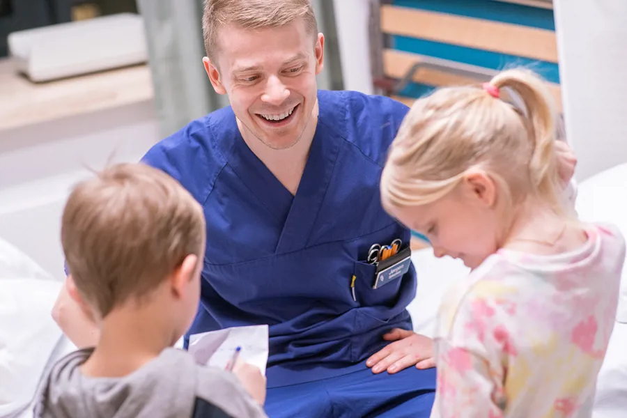 Mannlig sykepleier som smiler til to barn