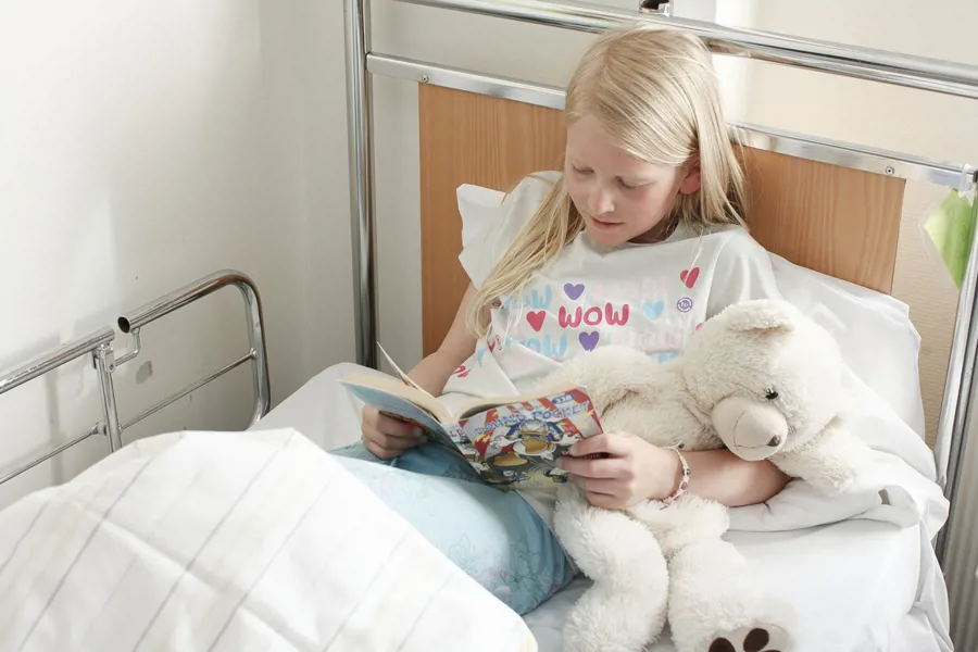 En jente som leser en bok i en sykehusseng