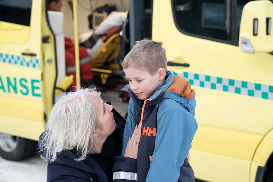 Mor som snakker med barn med ambulanse i bakgrunnen